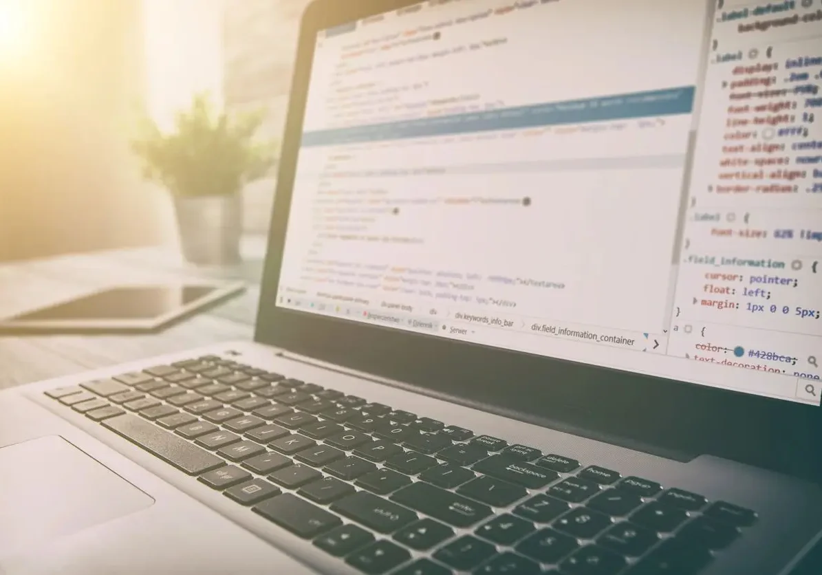 Close up view of laptop keyboard and screen from lower angle, screen shows various code
