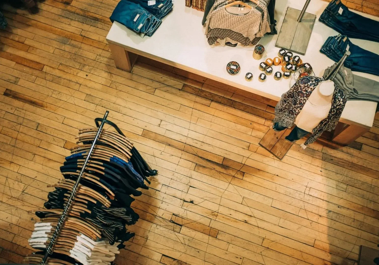 Overhead view of retail shop with wooden floors, one rack of clothes visible as well as a table with jeans and various accessories