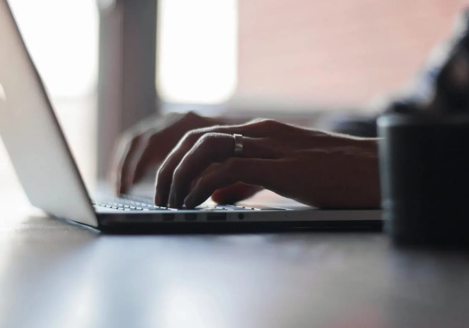 Close up of the left side of a laptop with a married man's hands typing, light in the background