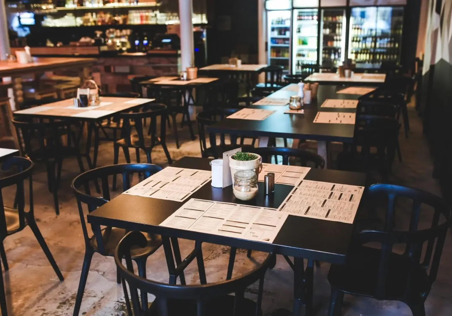 Empty market restaurant with tables and chairs, menus and condiments on table, beverage cooler shelves in background